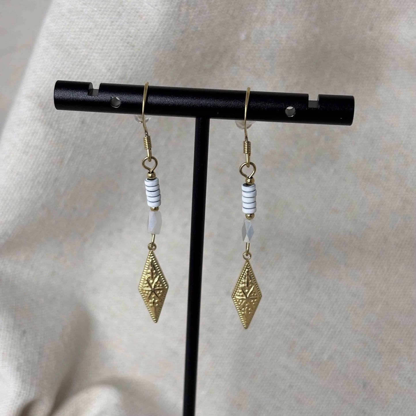 Boucles d'oreilles pendentif dorées avec perles plates blanches et breloque dorée rose des vents vendu sur le site internet prêtes à briller