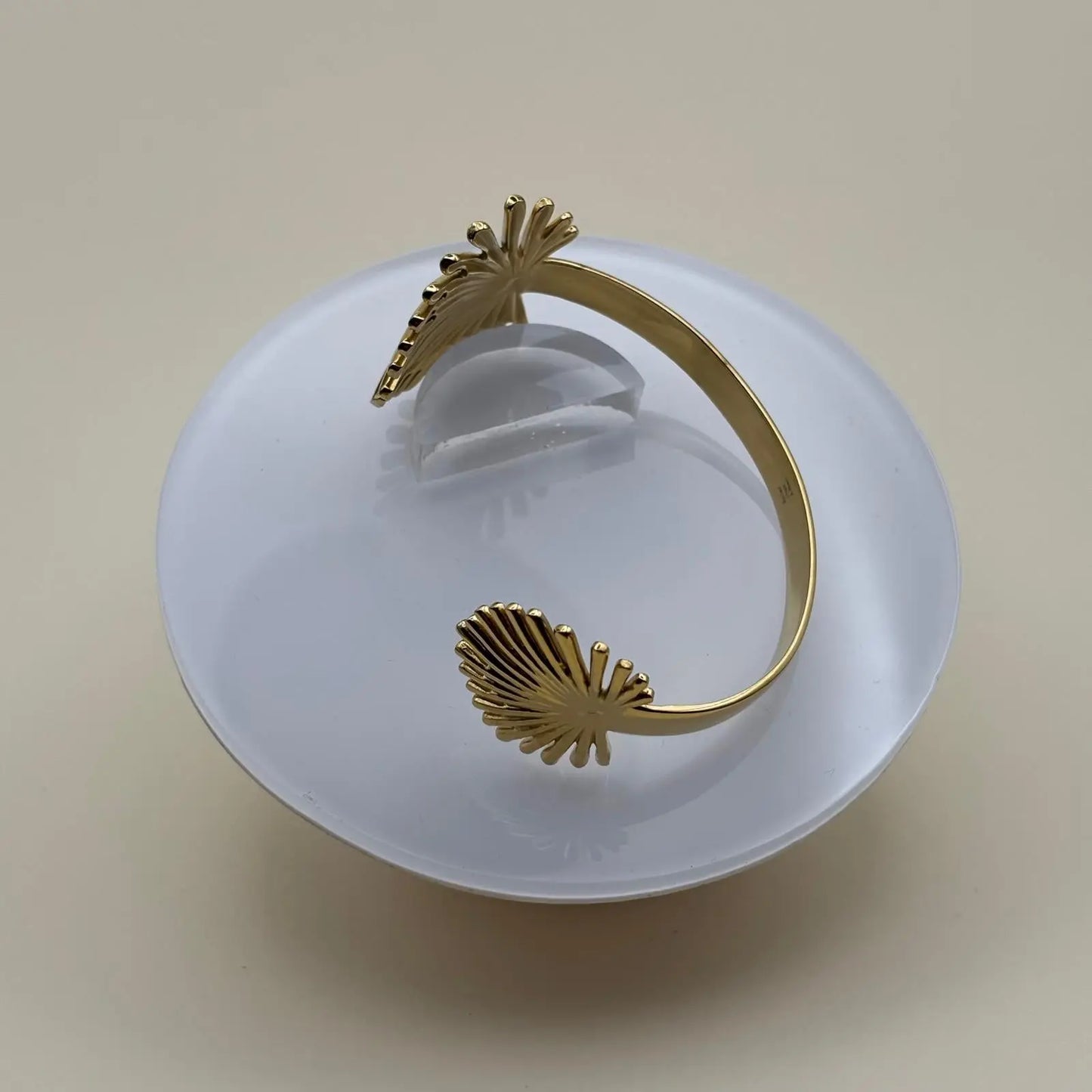 Vue de près d'un bracelet rigide doré ouvert avec motif feuille de palmier dorée
