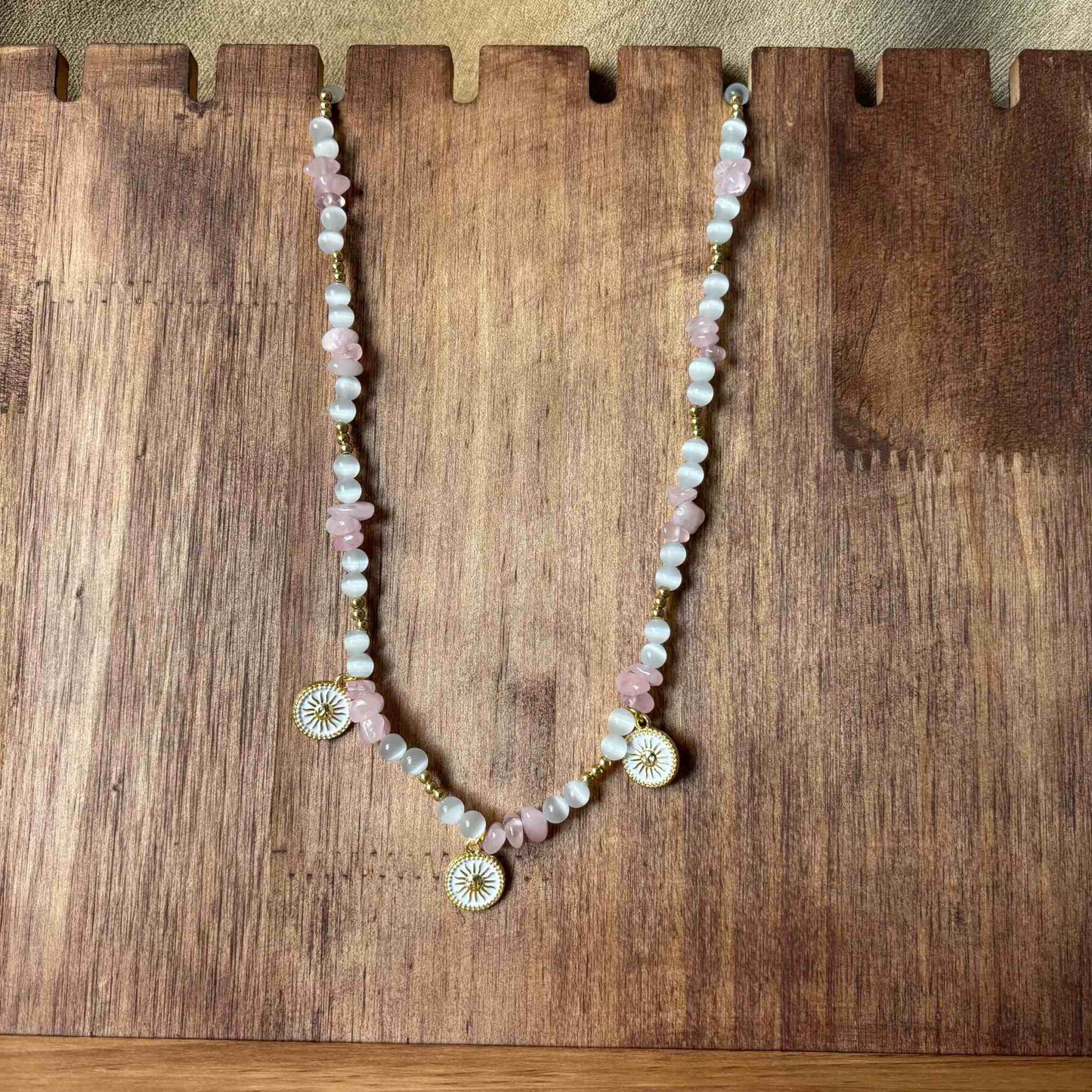 Vue de près d'un collier artisanal en perles rose et blanches avec pendentifs décoratifs en forme de soleil bijou vendu sur le site internet prêtes à briller