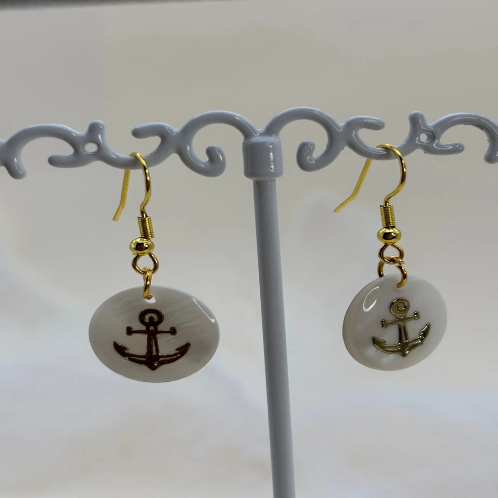 Une paire de boucles d'oreilles avec une pastille nacrée et dessin d'une ancre de marine