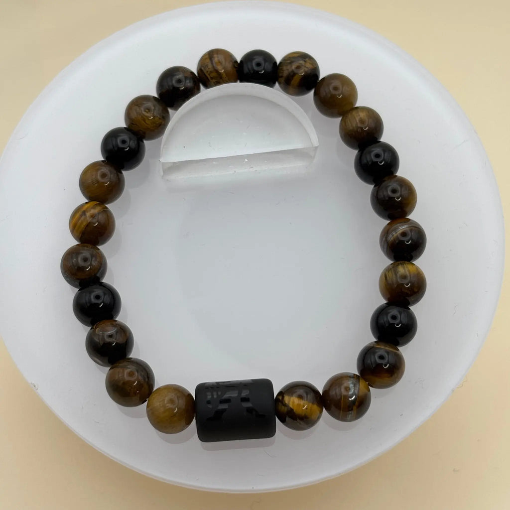 Bracelet de perles marron assorti d’anneaux argentés et d’un cylindre noir gravé en pièce centrale