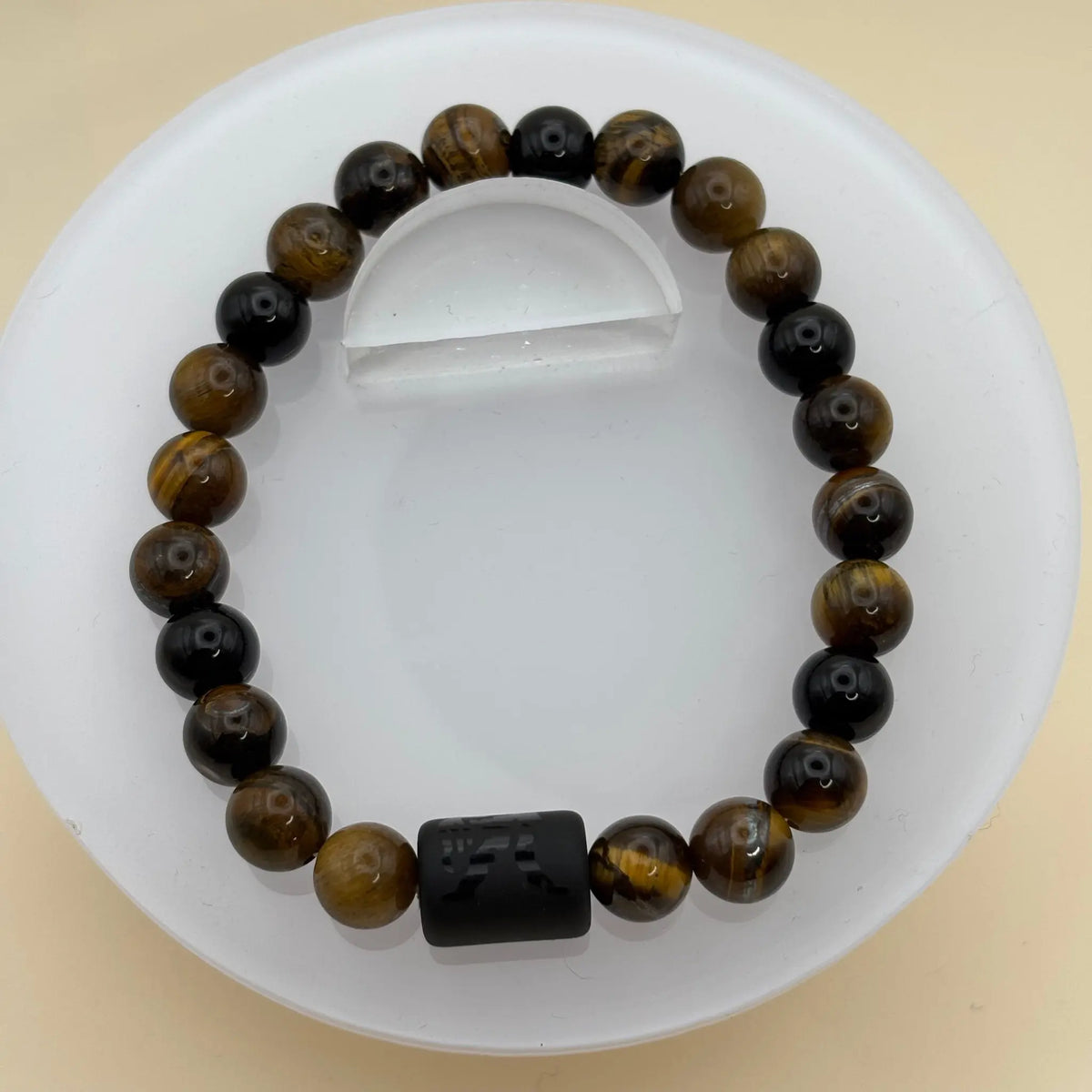 Bracelet de perles marron assorti d’anneaux argentés et d’un cylindre noir gravé en pièce centrale