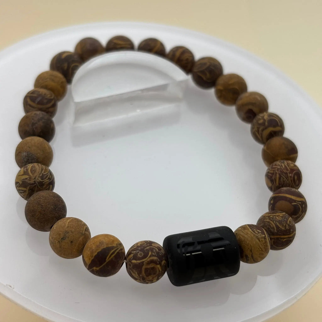 Bracelet aux nuances brunes, vertes et grises, rehaussé d’un médaillon argenté gravé