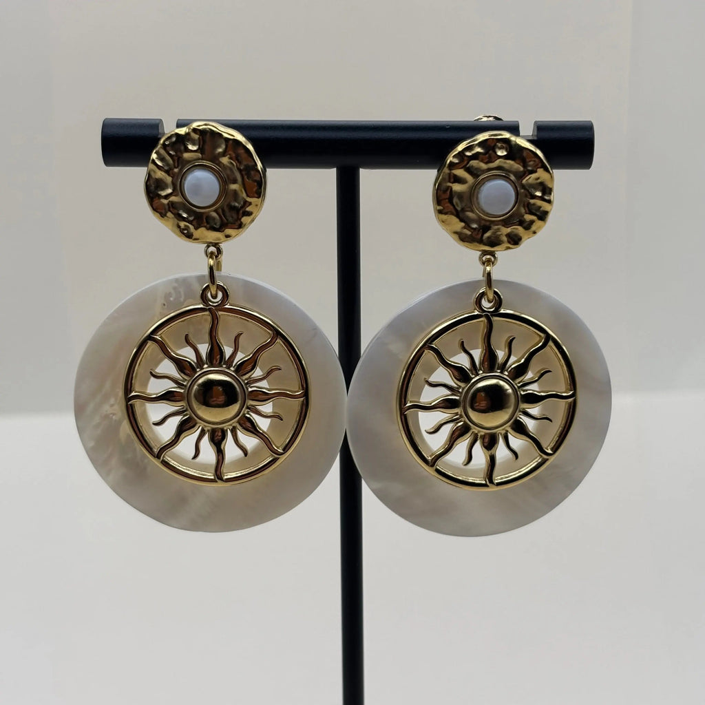 Des boucles d'oreilles dorées avec cercle blanc en nacre et motif de soleil 