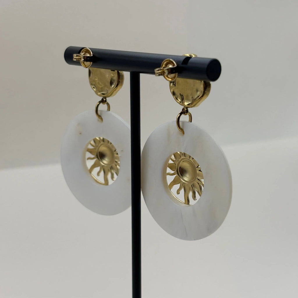 Des boucles d'oreilles de couleur dorées avec cercle blanc en nacre et motif de soleil 