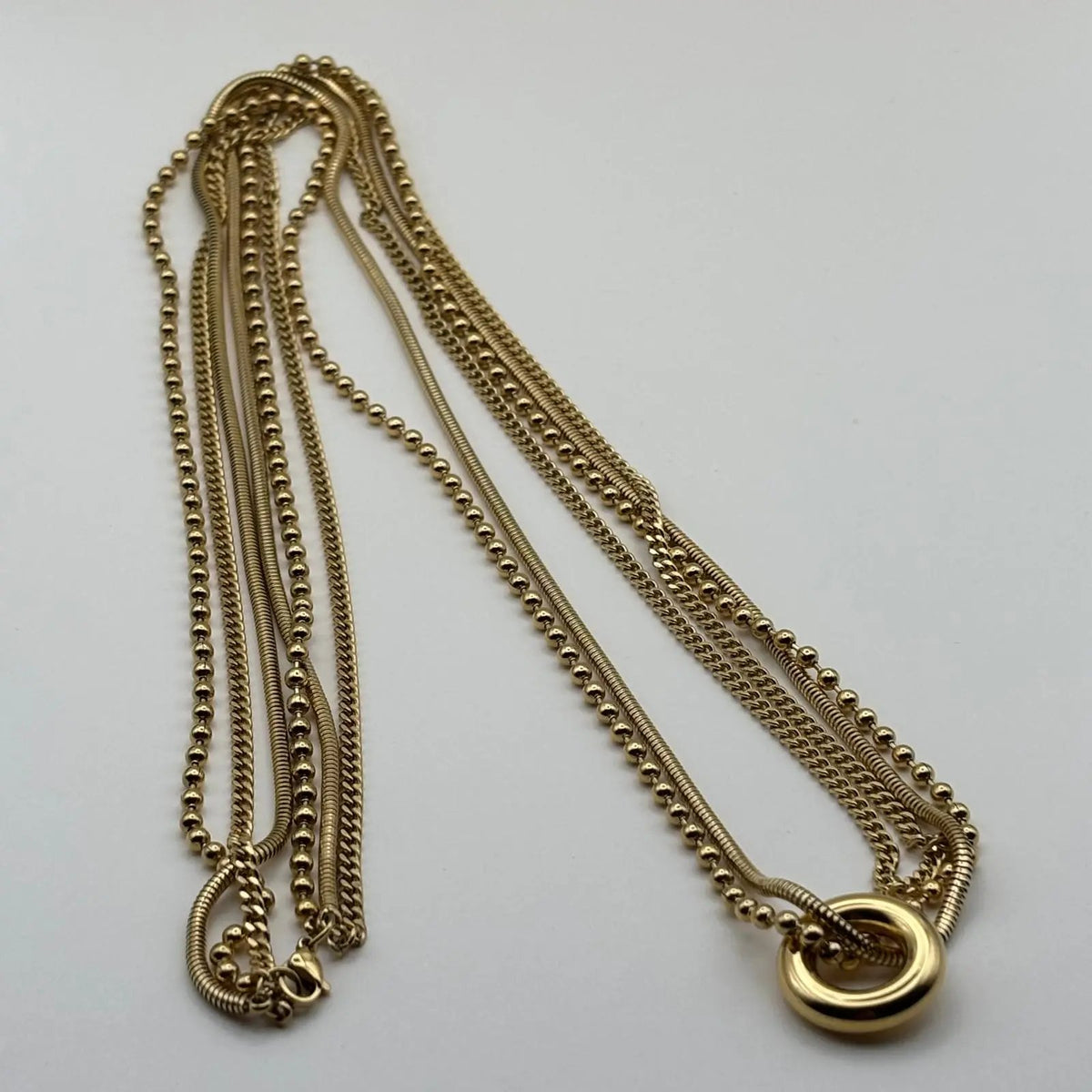 Un collier multirangs avec trois chaînes dorées et un anneau doré relié à deux chaines en acier inoxydable 
