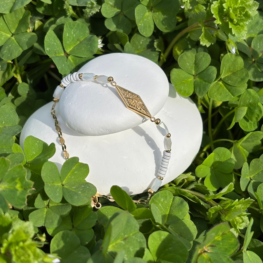 Un bracelet blanc  et or fantaisie sur un lit de trèfles