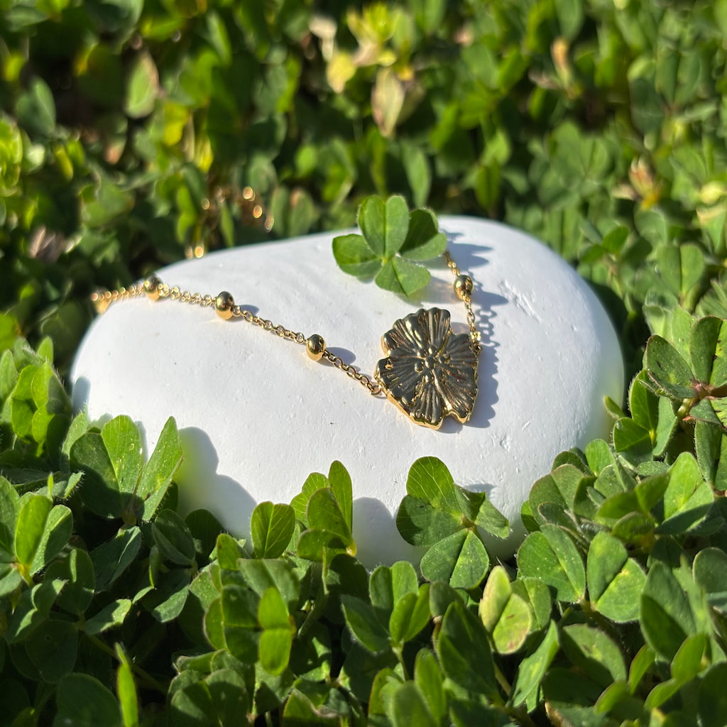 Un bracelet doré posé sur un galet blanc entouré de verdure