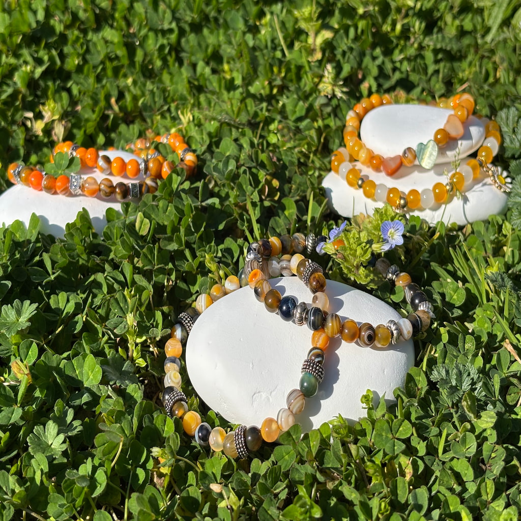 Un ensemble de trois bracelets artisanaux posé sur des galets blanc entouré de verdure