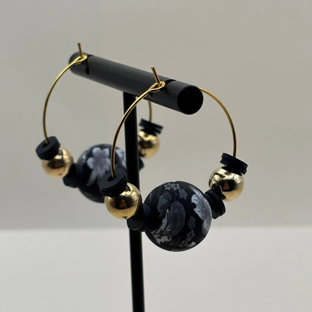 Une paire de boucles d'oreilles créole artisanales dorées avec breloque colorée et perles dorées et noires