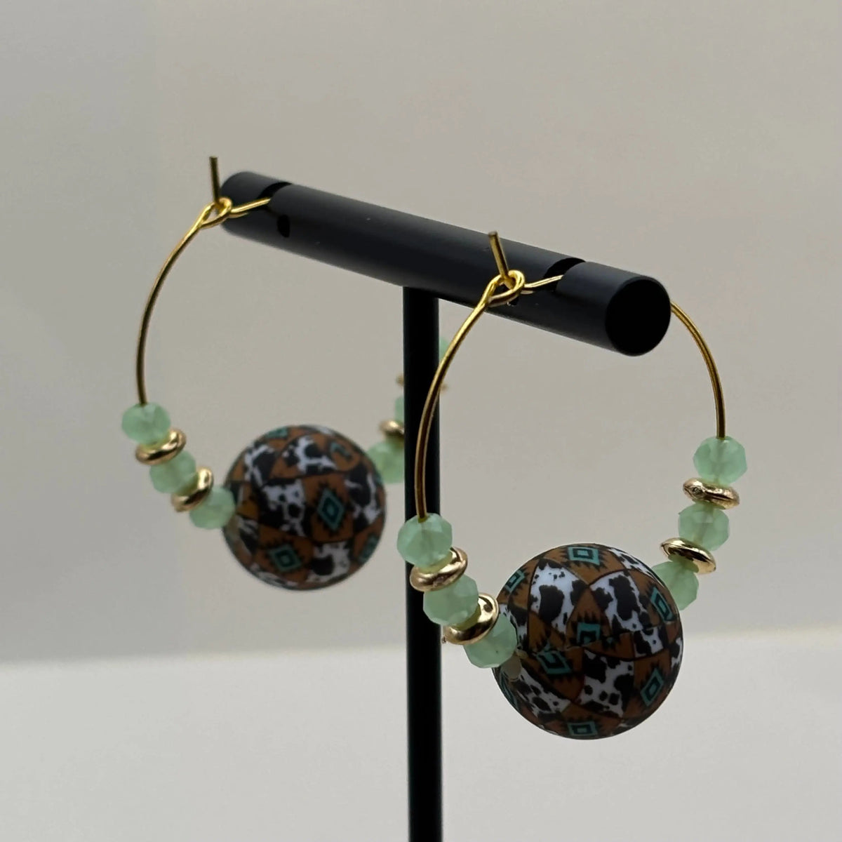 Une paire de boucles d'oreilles créole artisanales dorées avec breloque centrale colorée et perles vert d'eau