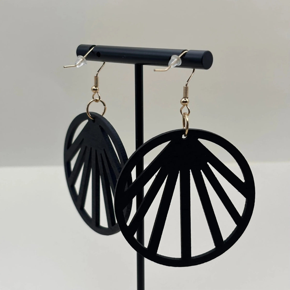Des boucles d'oreilles attache dorée et boucle en bois léger noire avec des motifs géométriques