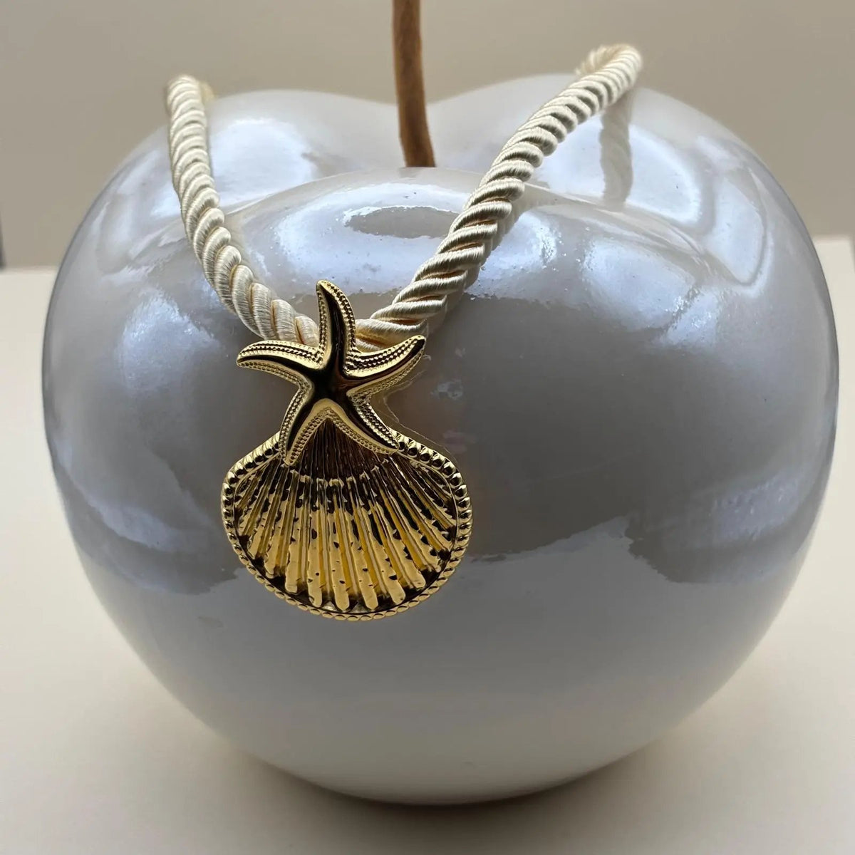 Collier fantaisie sur une corde nylon écrue avec un pendentif coquillage doré 