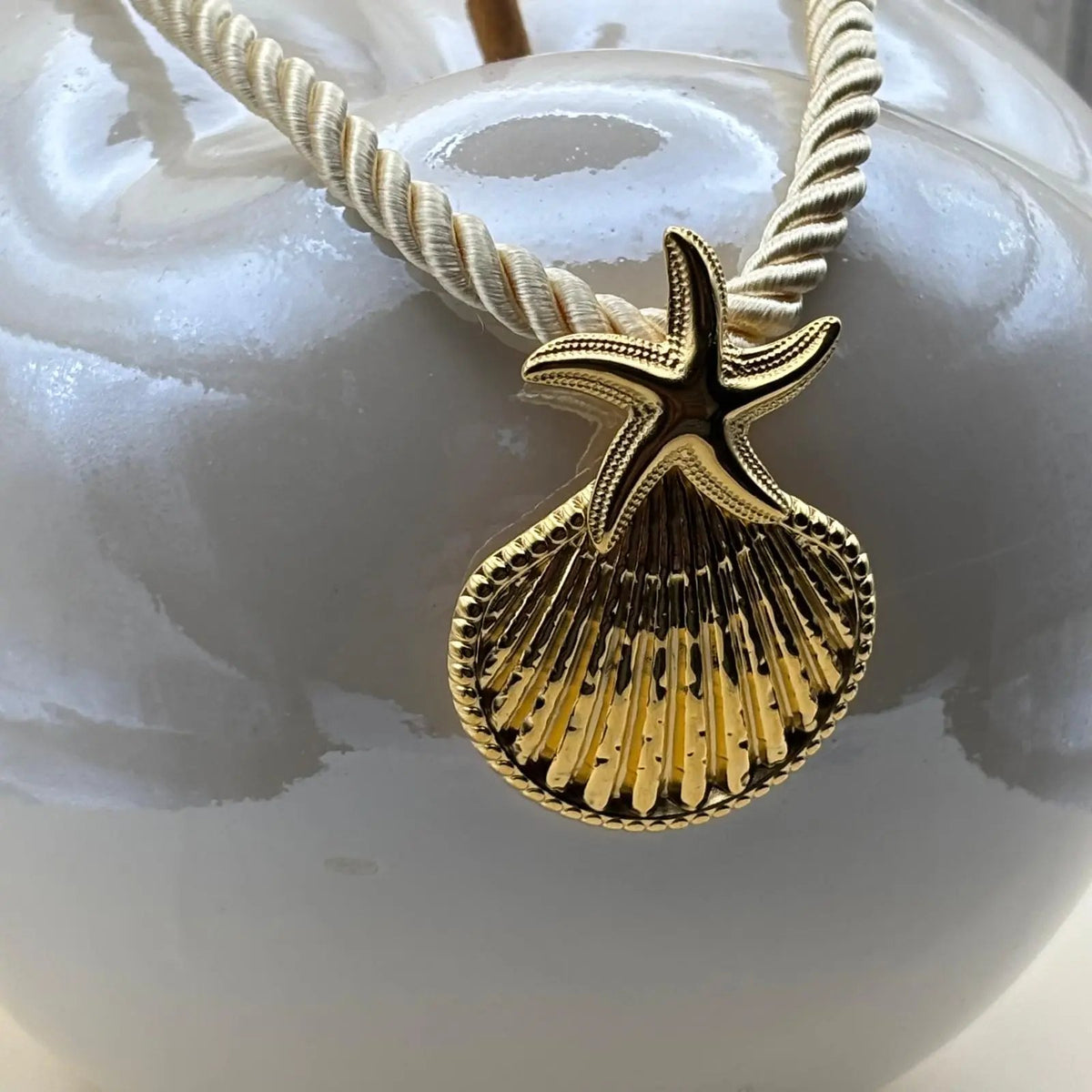 Collier fantaisie sur une corde en nylon écrue avec un pendentif coquillage doré 