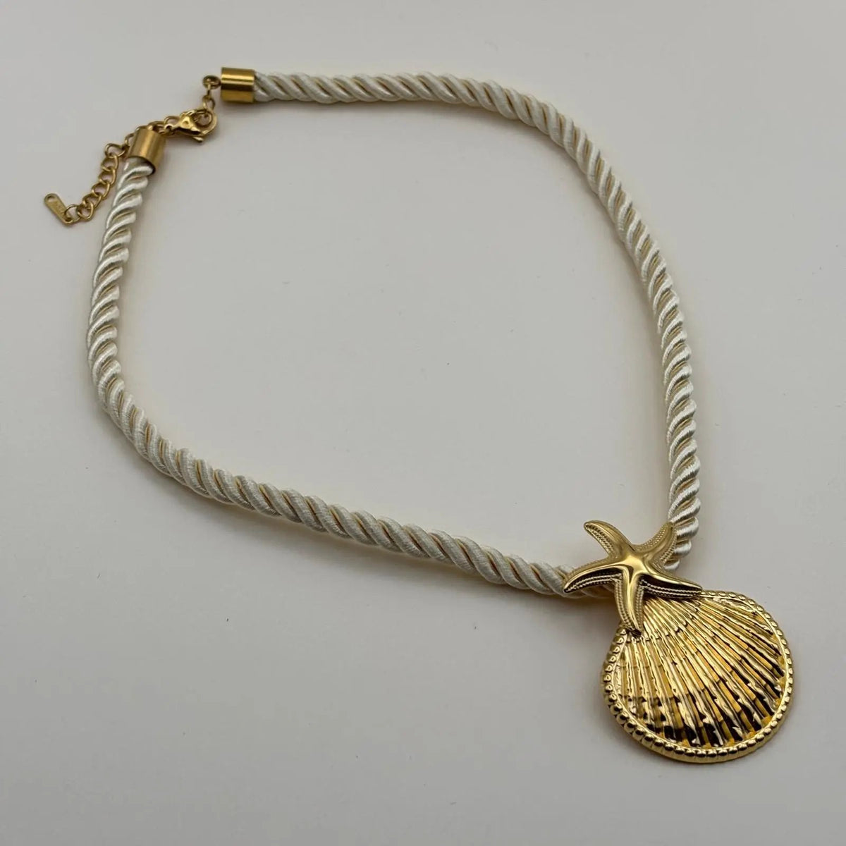 Un collier fantaisie sur une corde nylon écrue avec un pendentif coquillage doré 