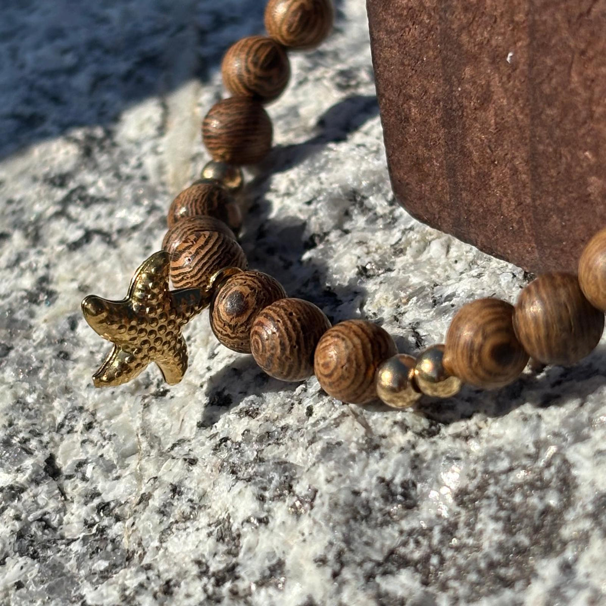 Vue de près d'un bracelet en perles artisanal avec une breloque étoile de mer dorée  et des perles en bois sur élastique