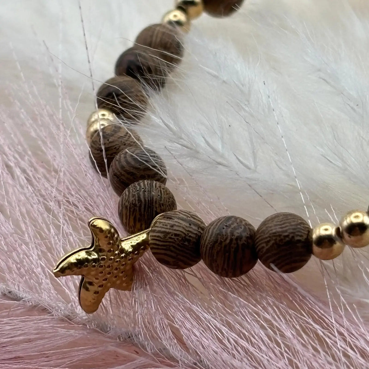 Vue de près d'un bracelet en perles artisanal avec une breloque étoile de mer dorée  et des perles en bois sur élastique sur le site internet prêtes à briller