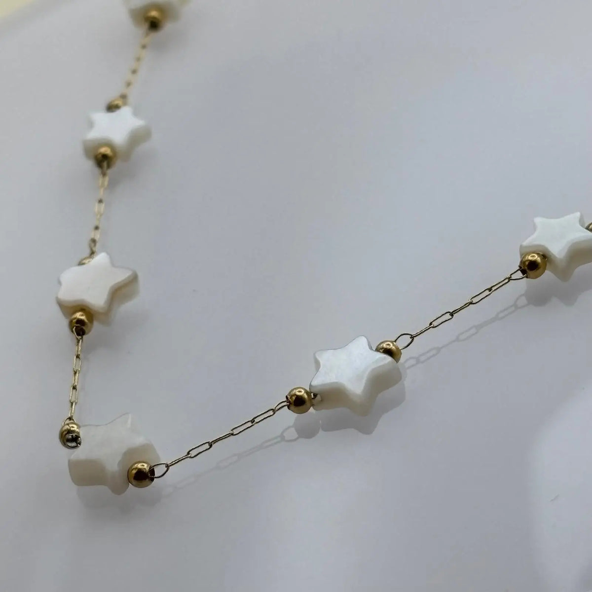 Bracelet doré à petits maillons avec des breloques en forme d'étoiles blanches 