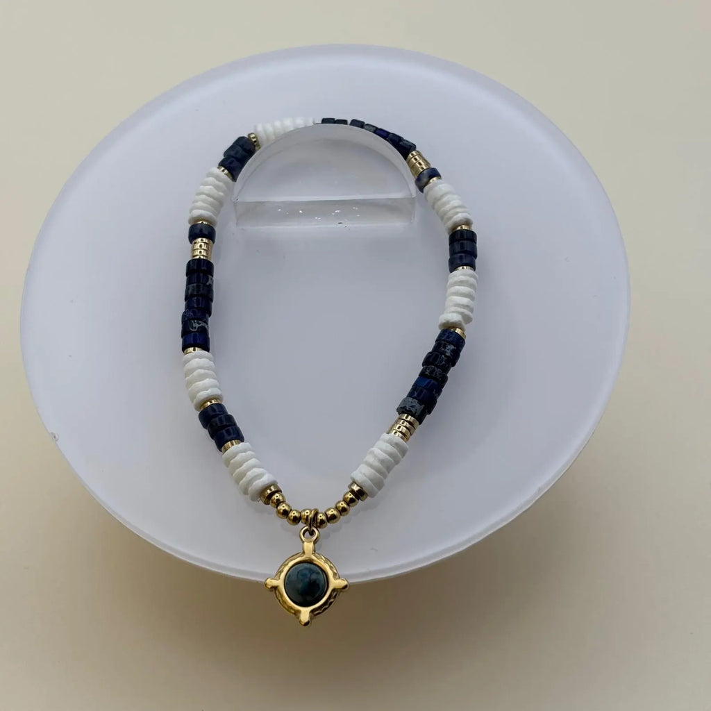 Bracelet en perles artisanal avec une breloque dorée et une pierre bleue et des perles acryliques blanches et bleues sur élastique