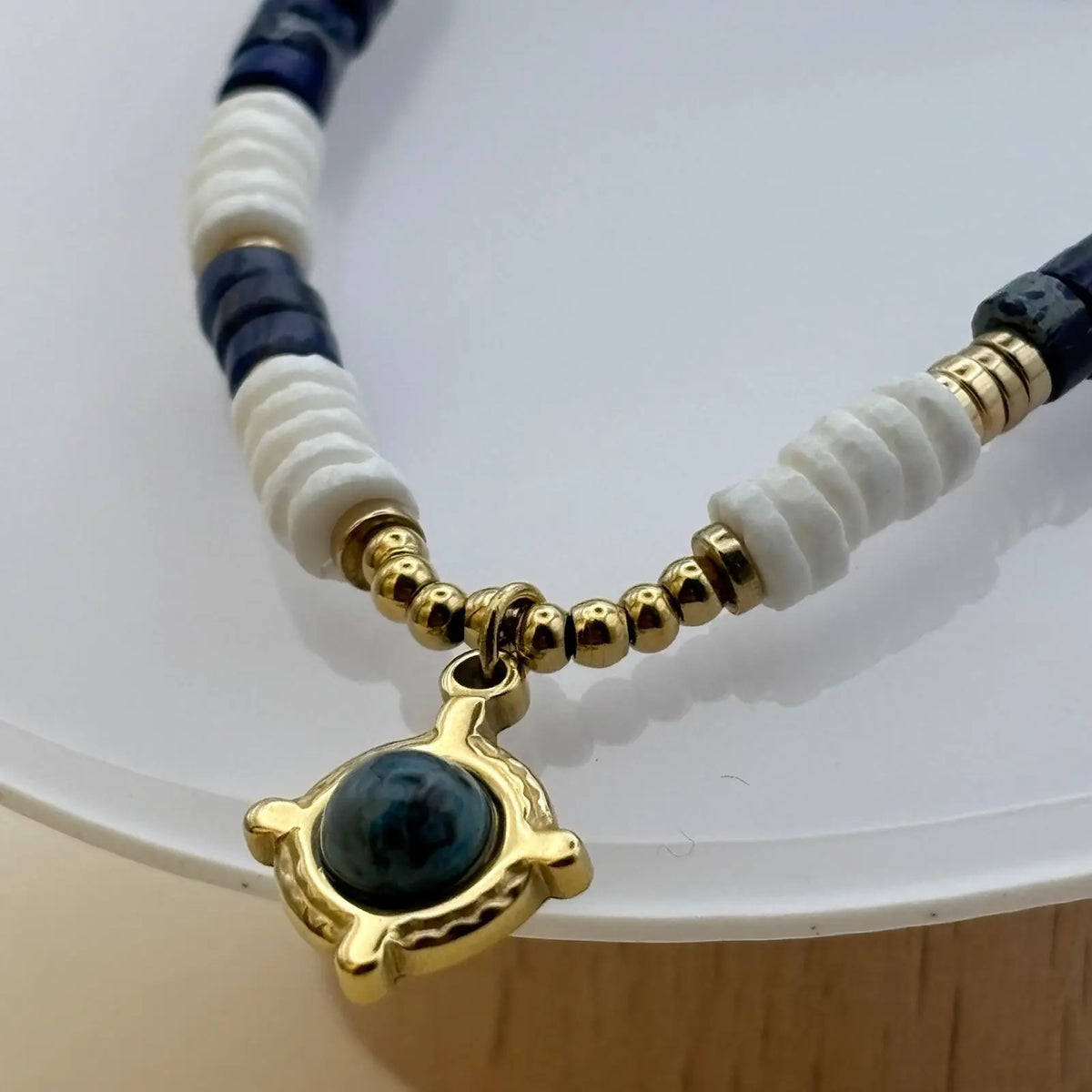 Bracelet en perles artisanal avec breloque dorée et une pierre bleue et des perles acryliques blanches et bleues sur élastique