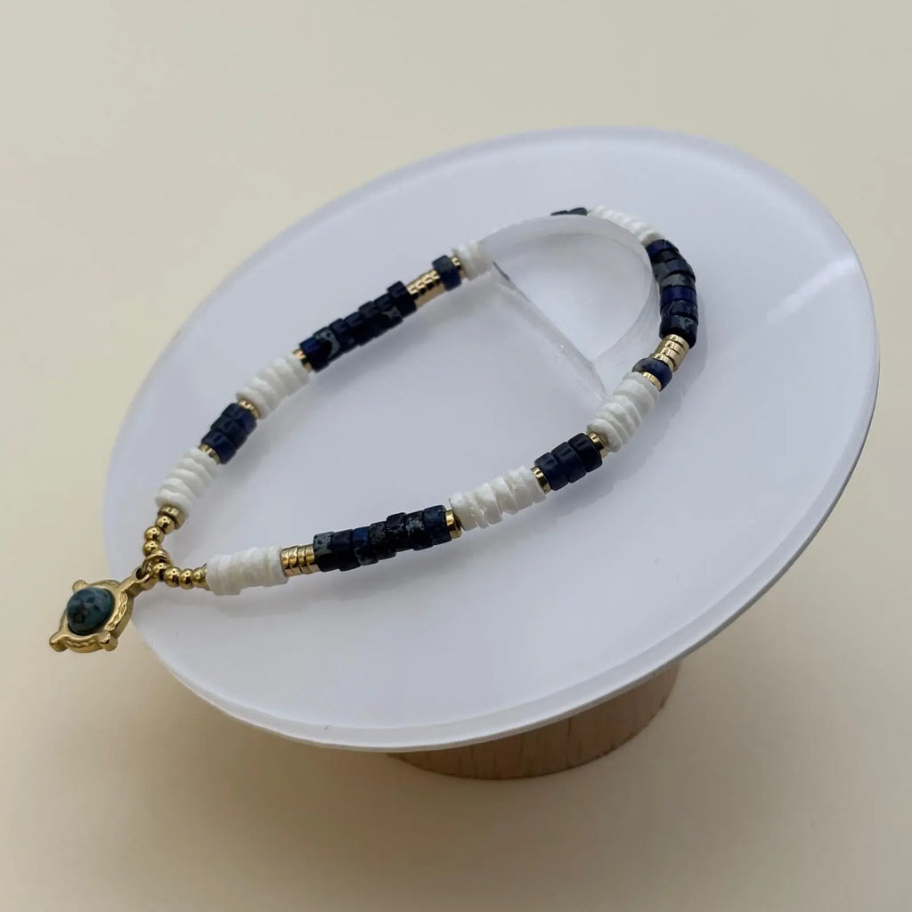 Bracelet en perles artisanal avec une breloque dorée et une pierre bleue des perles acryliques blanches et bleues sur élastique