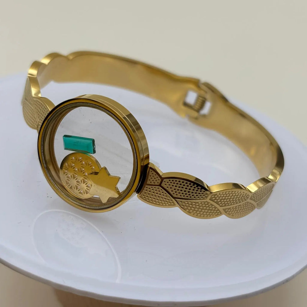 Bracelet doré à jonc ouvert avec cercle central transparent rempli d'éléments décoratifs et ouverture par le dessous en acier inoxydable