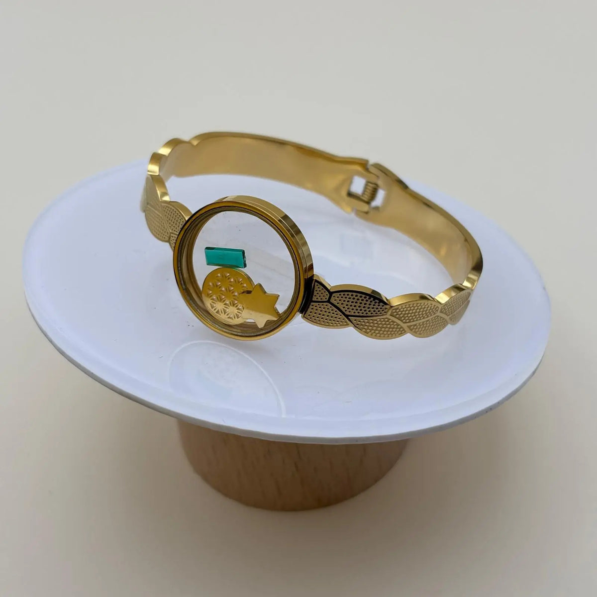 Bracelet doré à jonc ouvert avec cercle central transparent rempli d'éléments décoratifs et ouverture par le dessous en acier inoxydable doré