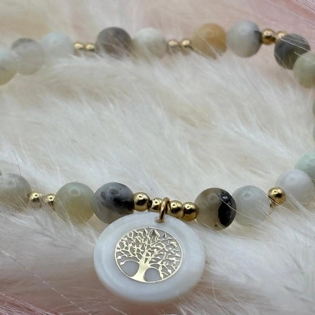 Vue de près d'un bracelet en perles artisanal avec breloque pastille en nacre motif arbre de vie et perles naturelles pastels sur élastique