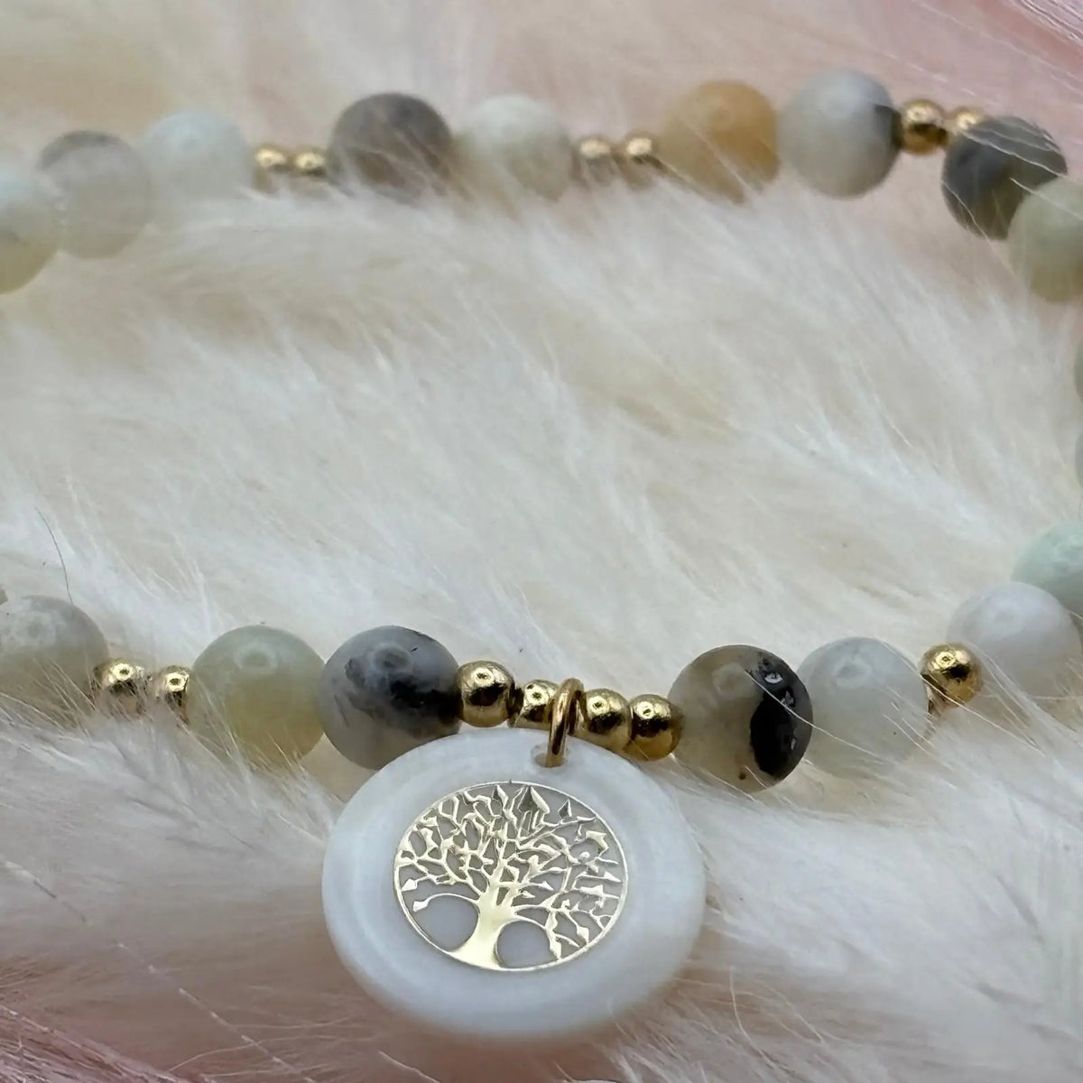 Vue de près d'un bracelet en perles artisanal avec breloque pastille en nacre motif arbre de vie et perles naturelles pastels sur élastique