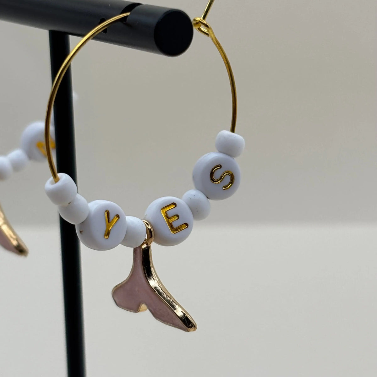 Des boucles dorées à perles blanches et queux de baleine roses suspendues et les mots oui et non inscrit sur des perles 