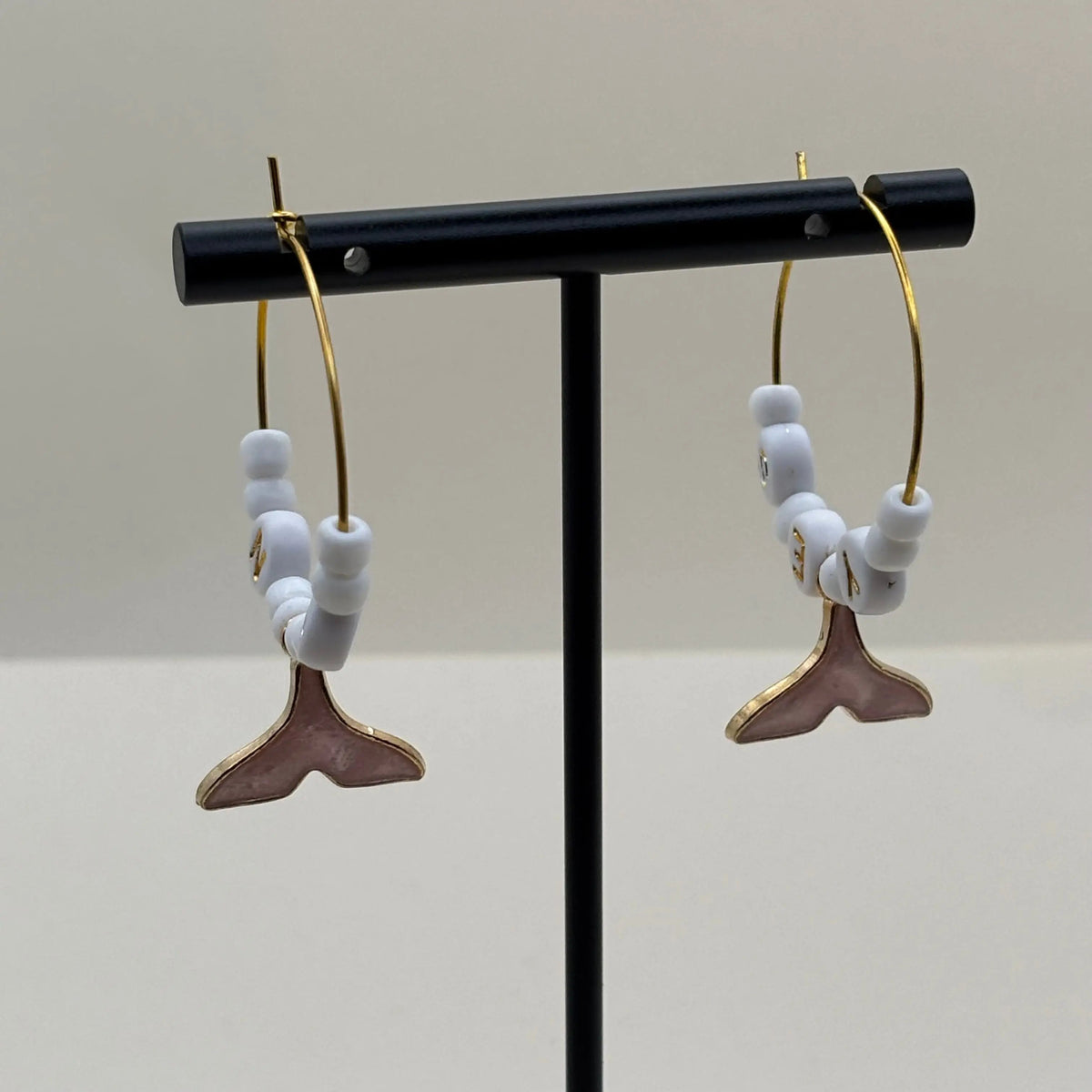 Une paire de boucles dorées à perles blanches et queux de baleine roses suspendues et les mots oui et non inscrit sur des perles 