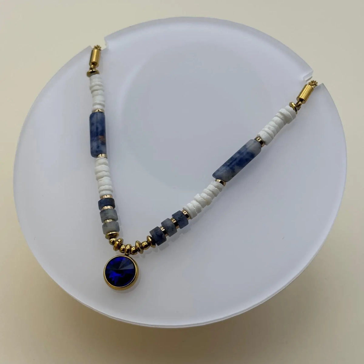 Bracelet doré avec des perles acryliques blanches et bleues et un médaillon de couleur bleu profond