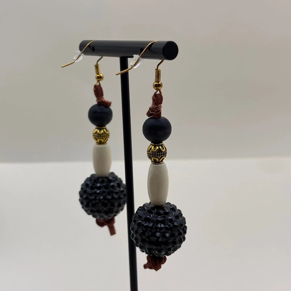Des boucles d'oreilles pendantes dorées, grosse perle noire et perle allongée blanche 