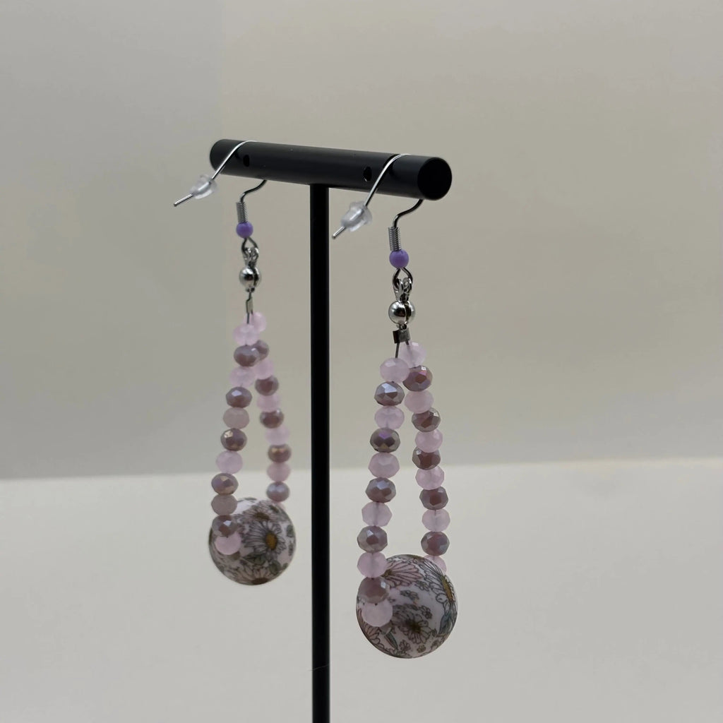 Une paire de boucles d'oreilles pendentif avec des petites perles mauves et une grosse perle fleurie 