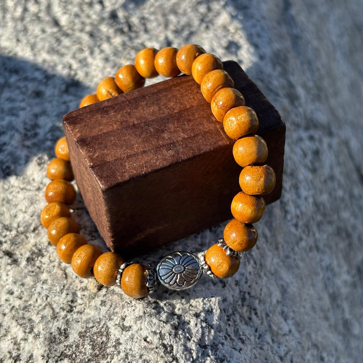 Bracelet en perles artisanal avec une breloque en forme de fleur argentée et des perles en bois