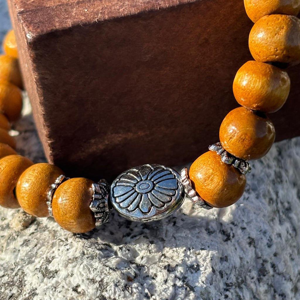 Vue de près d'un bracelet en perles artisanal avec une breloque en forme de fleur argentée et des perles en bois