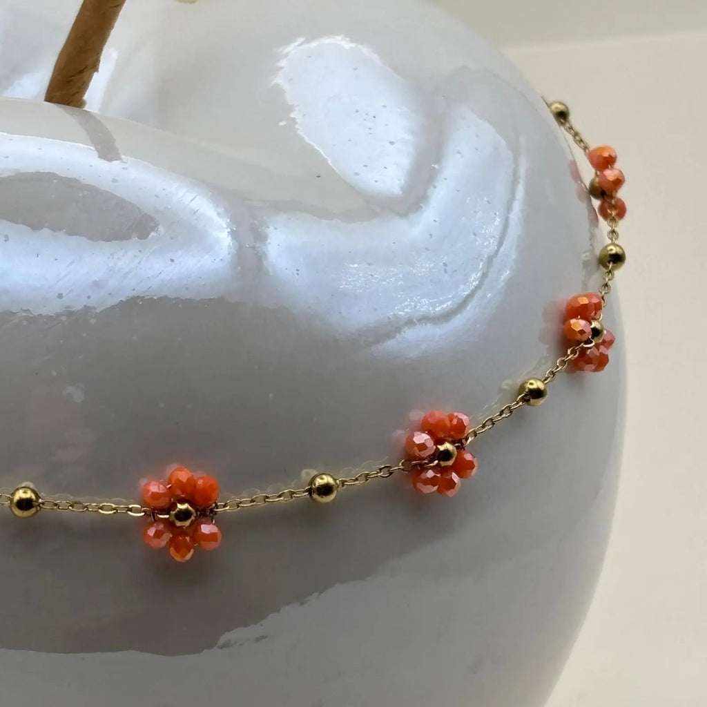 Un collier fantaisie avec une chaine dorée à petits maillons et des fleurs colorées orange la chaine est en acier inoxydable 