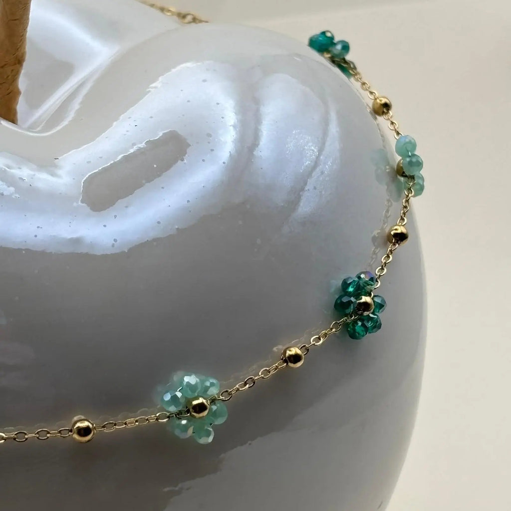 Un collier fantaisie avec une chaine dorée à petits maillons et des fleurs colorées orange la chaine est en acier inoxydable 