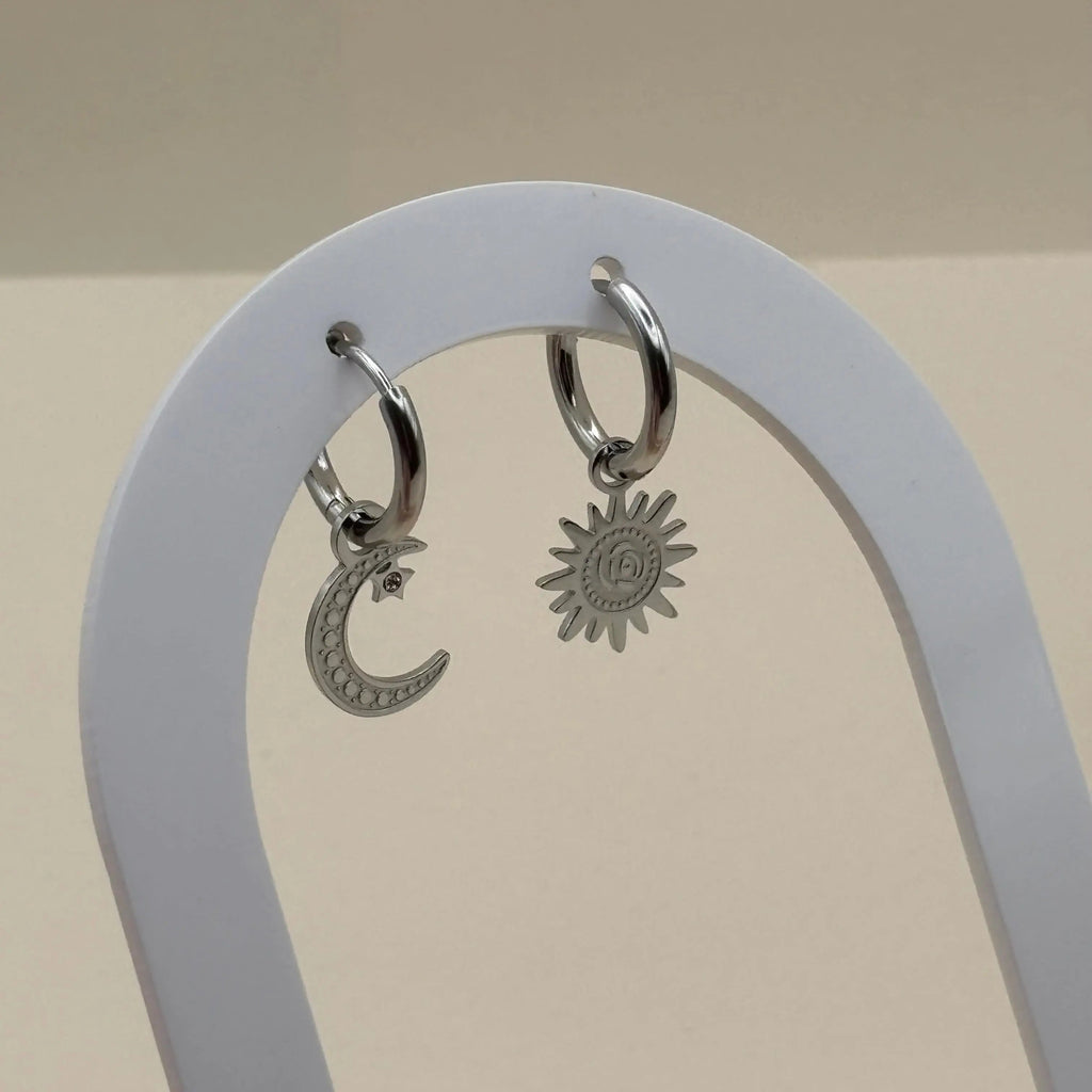 Une paire de boucles d'oreilles argentées en petites créoles asymétrique lune et soleil  en acier inoxydable 