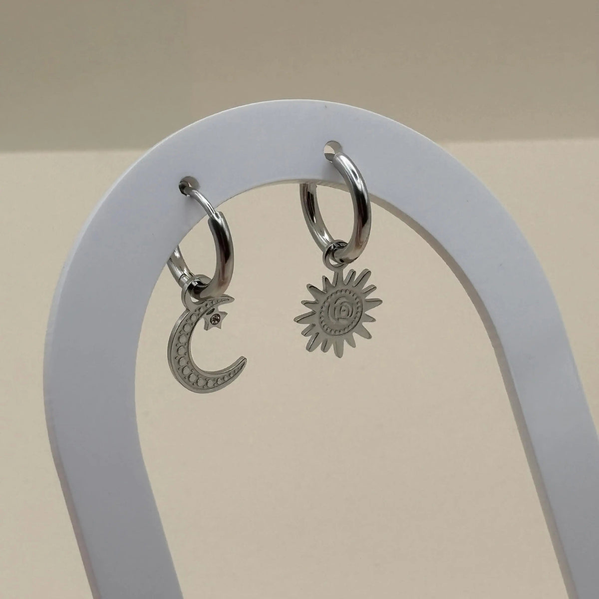 Une paire de boucles d'oreilles argentées en petites créoles asymétrique lune et soleil  en acier inoxydable 