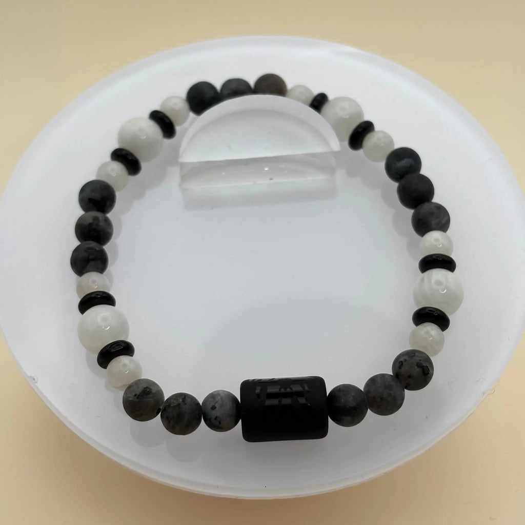 Bracelet multicolore mêlant tons verts, bruns et gris, avec une pièce centrale argentée gravée