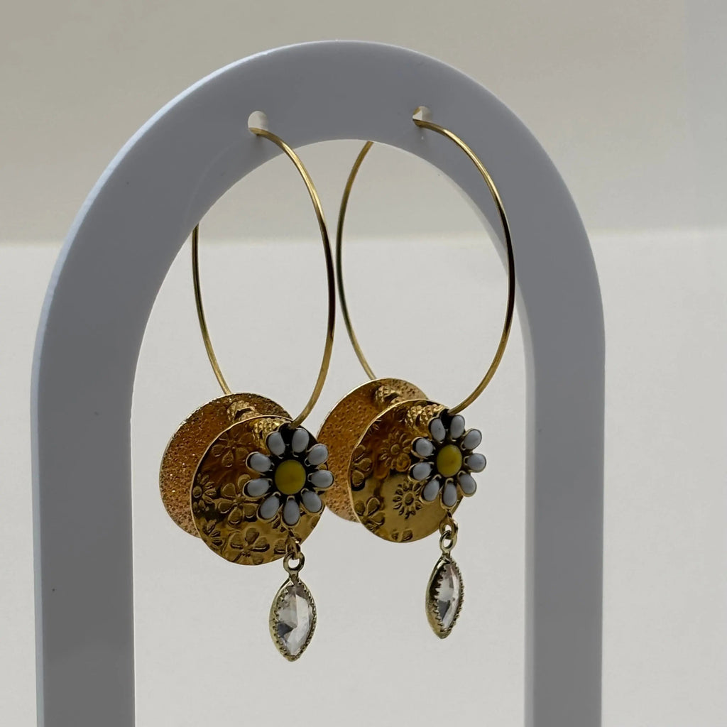 Une paire de boucles d'oreilles créoles dorées avec pendentif pastille dorée avec une fleur marguerite et des perles