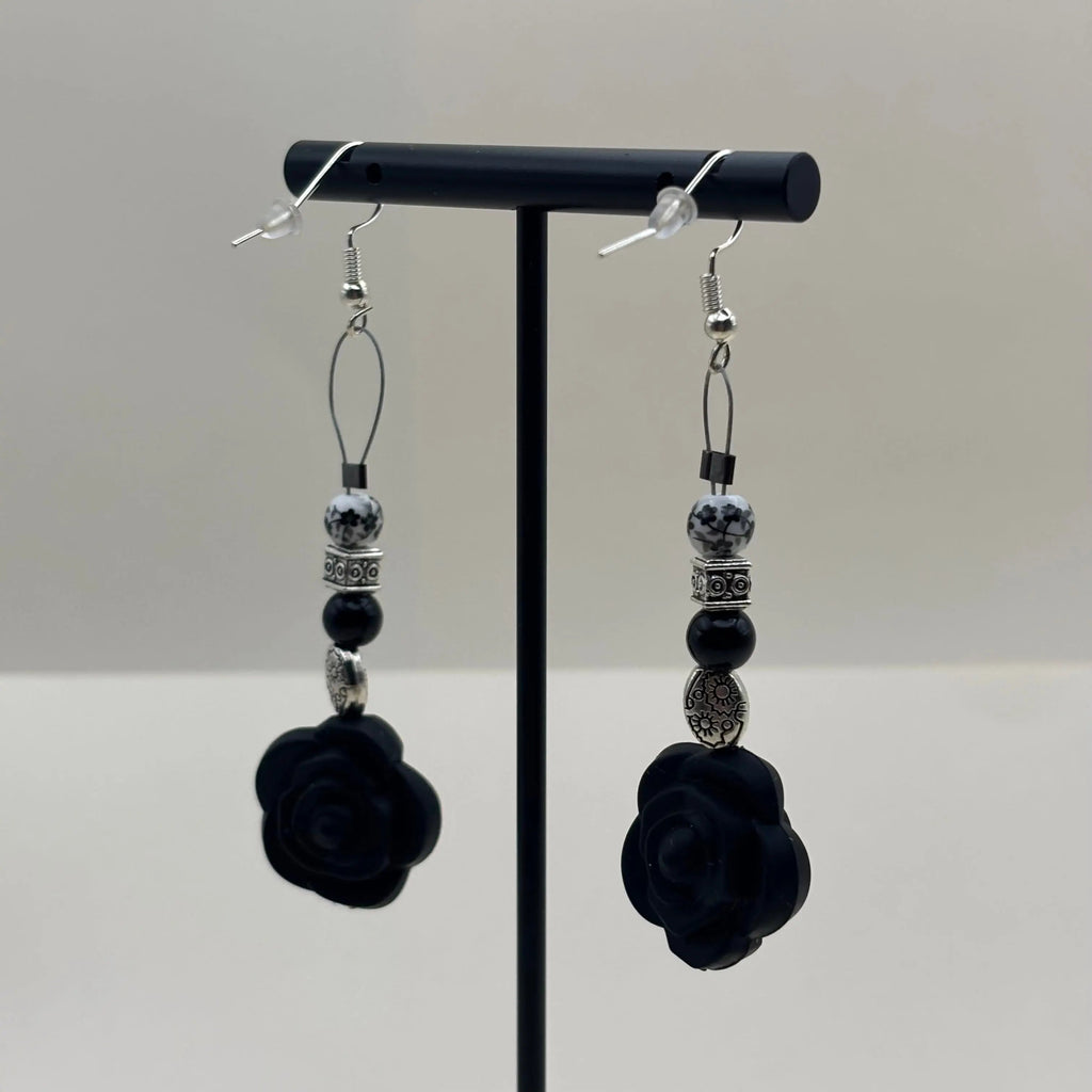 Des boucles d'oreilles artisanales avec fixation argentée un breloque en forme de fleur noire et différentes perles 