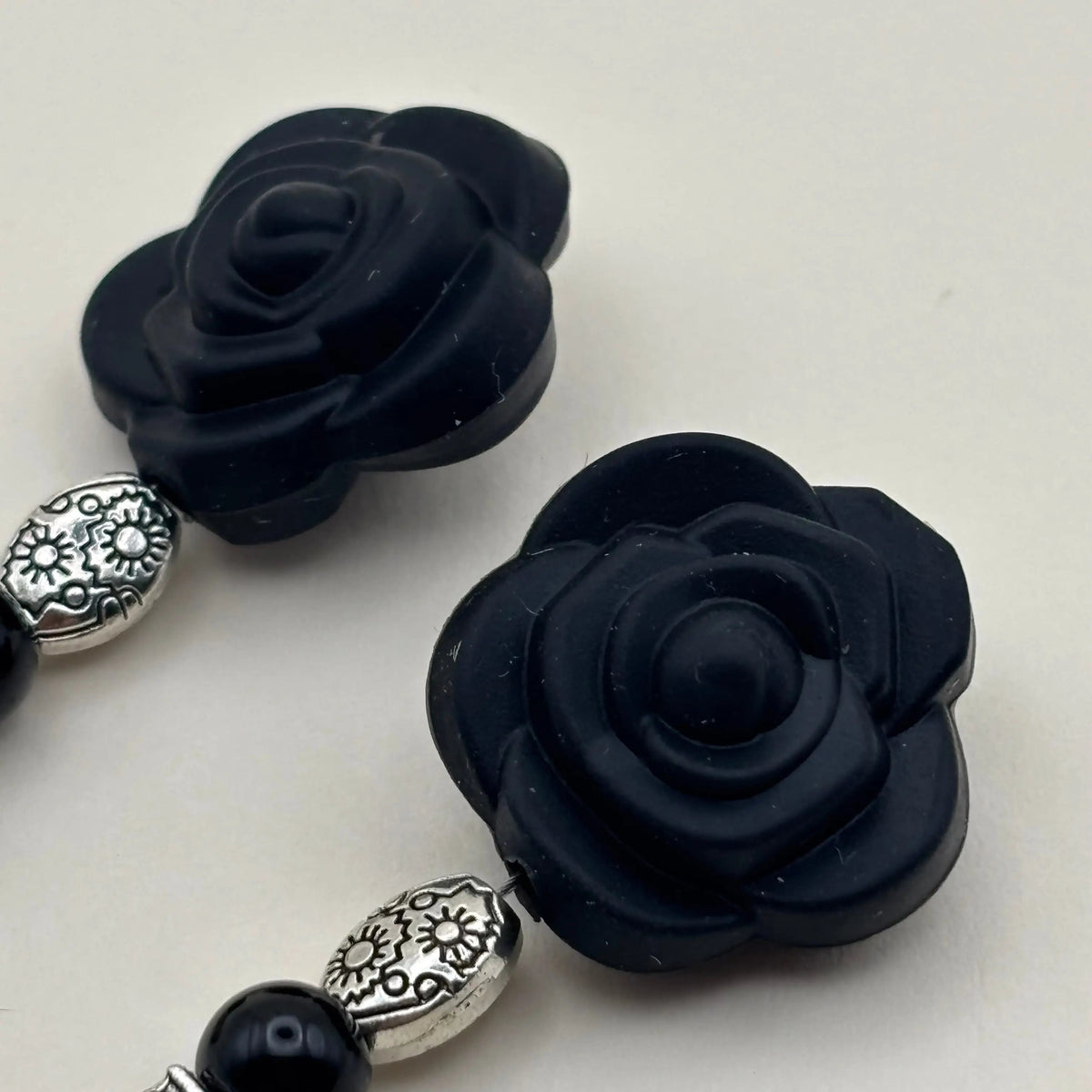 Une paire de boucles d'oreilles artisanales avec fixation argentée un breloque en forme de fleur noire et différentes perles 