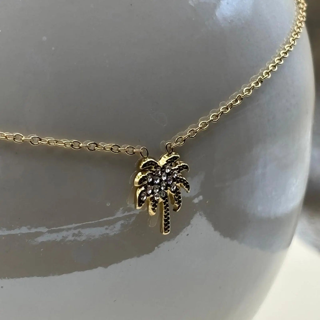 Collier de couleur dorée et bracelet à petits maillons avec une breloque en forme de palmier avec des strass 