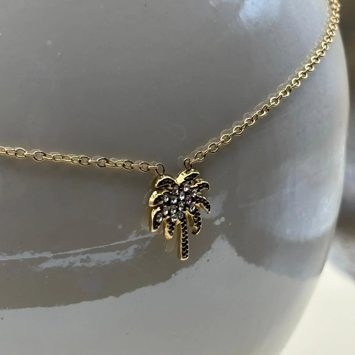 Collier de couleur dorée et bracelet à petits maillons avec une breloque en forme de palmier avec des strass 