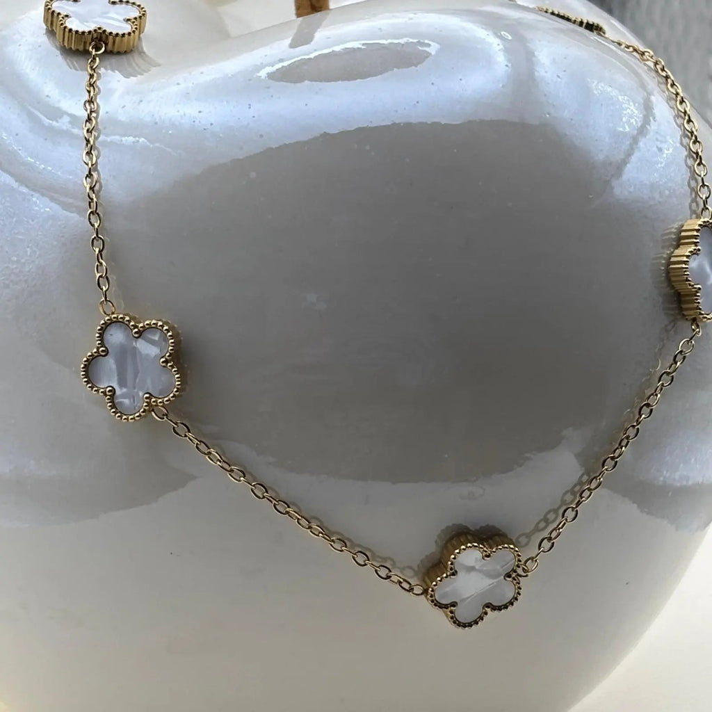 Un collier doré avec de fins maillons et des fleurs colorées blanches en acier inoxydable