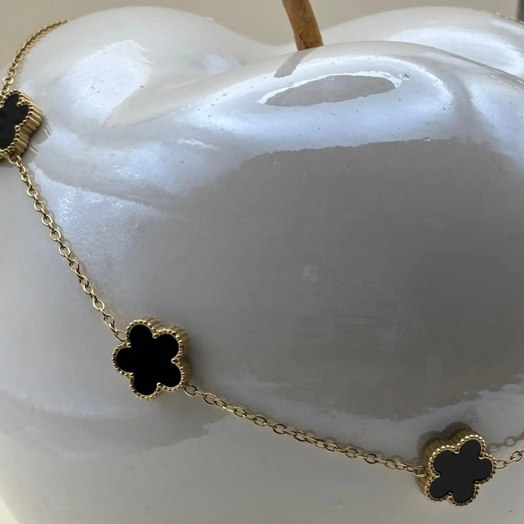 Un collier doré avec de fins maillons et des fleurs colorées noires en acier inoxydable