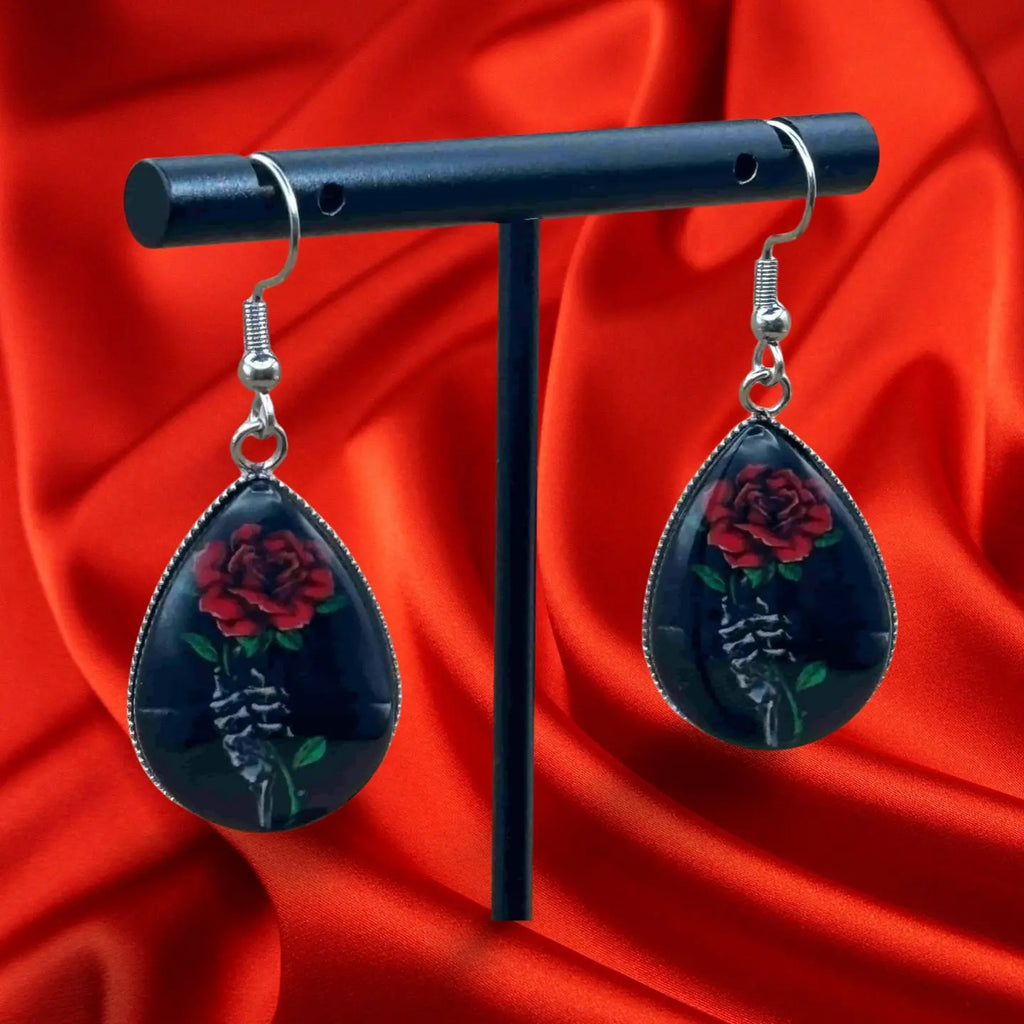 Boucles d'oreilles pendentif halloween en forme de goutte noire avec à l'intérieur une rose rouge et une main squelette vendues sur le site pretes a briller