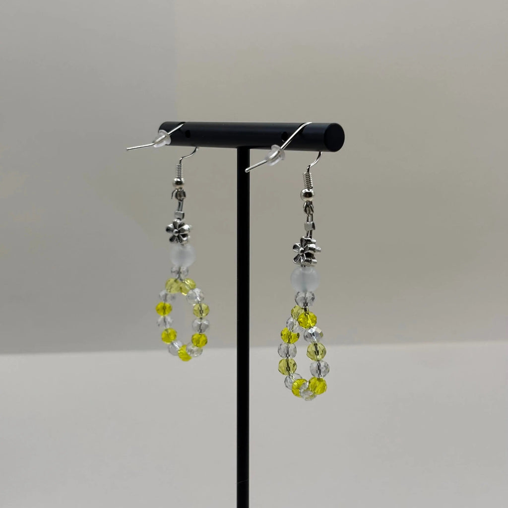 Une paire de boucles d'oreilles pendentif avec des perles acryliques blanches et une couronne en perles jaune et blanches